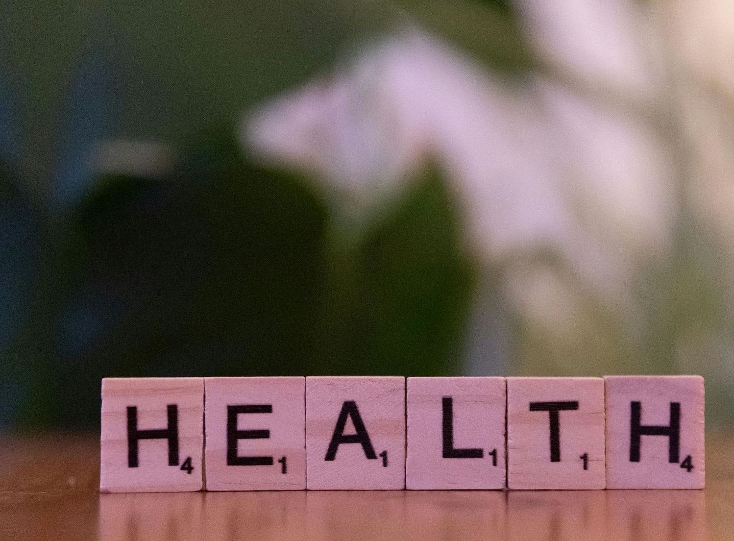 The word health is written in scrabble tiles on a wooden table.