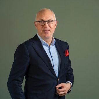a man in a suit and glasses is standing with his hands in his pockets .