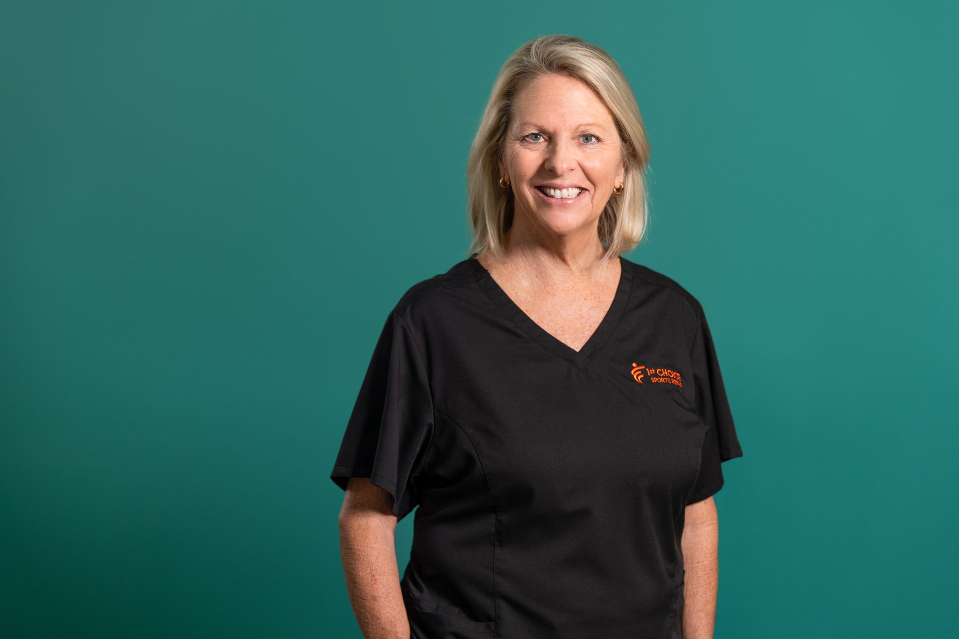 Woman in black scrubs smiling, standing against a teal background.