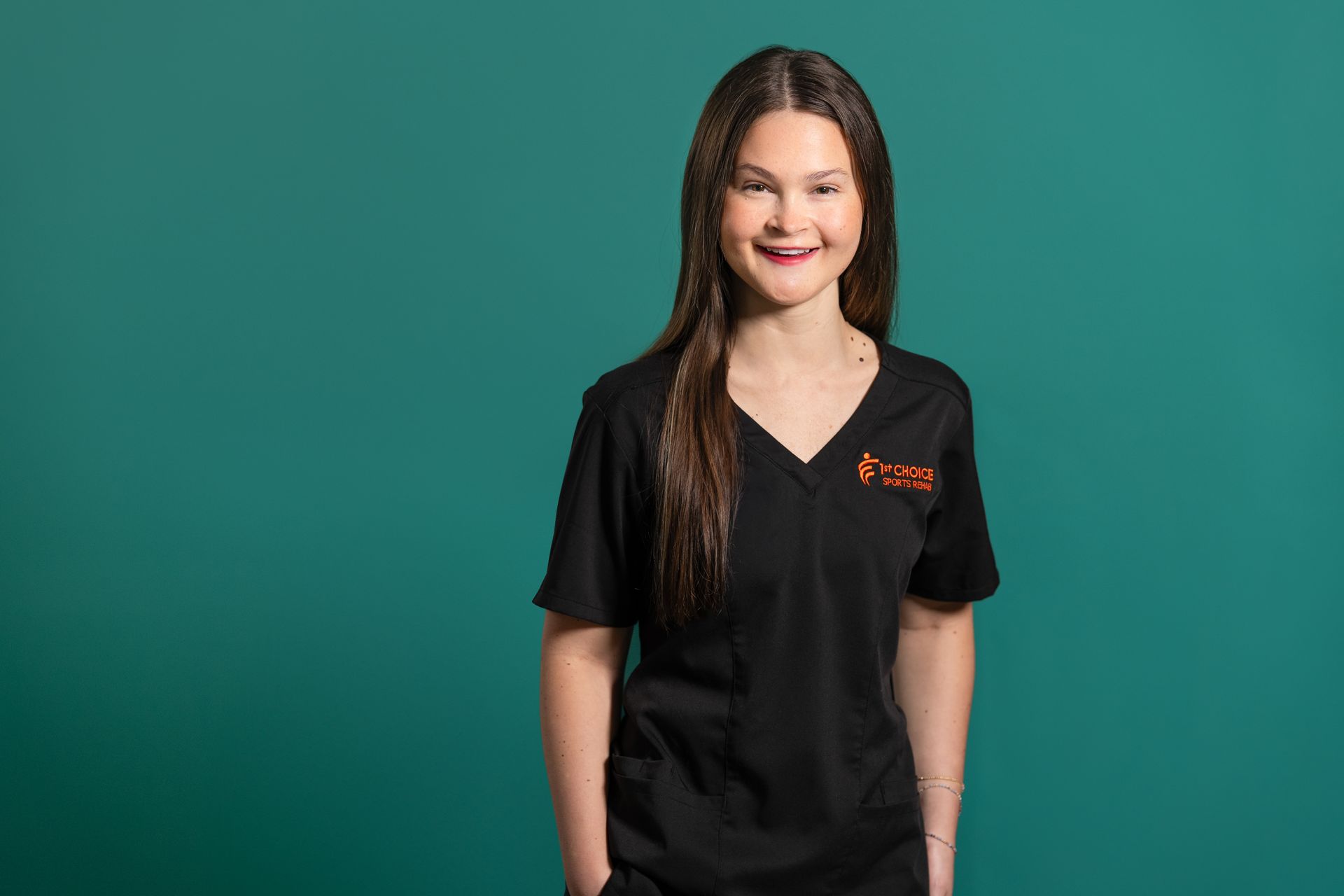 Woman in black scrubs smiles against a teal background.