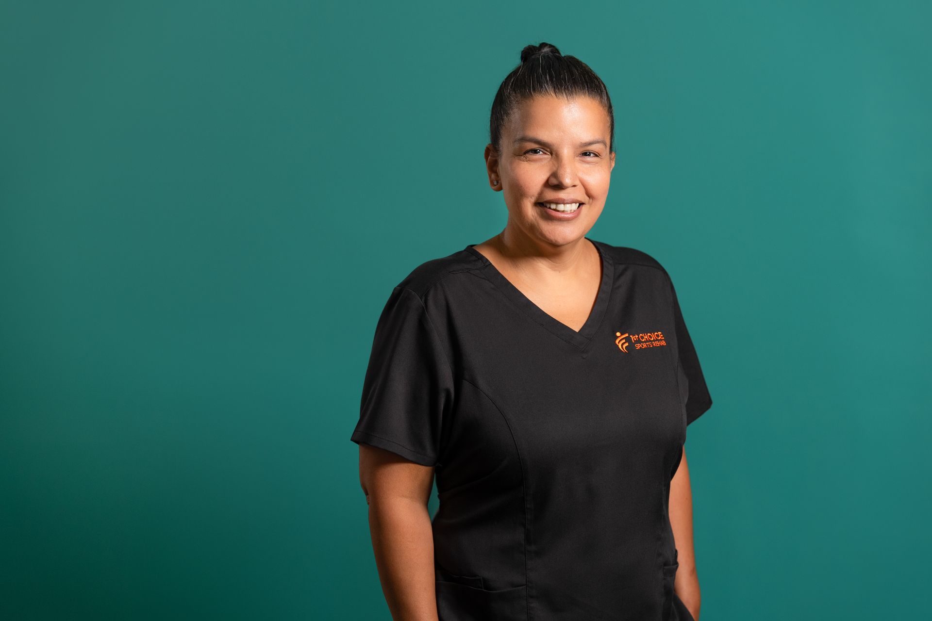 Woman in black scrubs smiles, against a teal background. Logo on the chest.