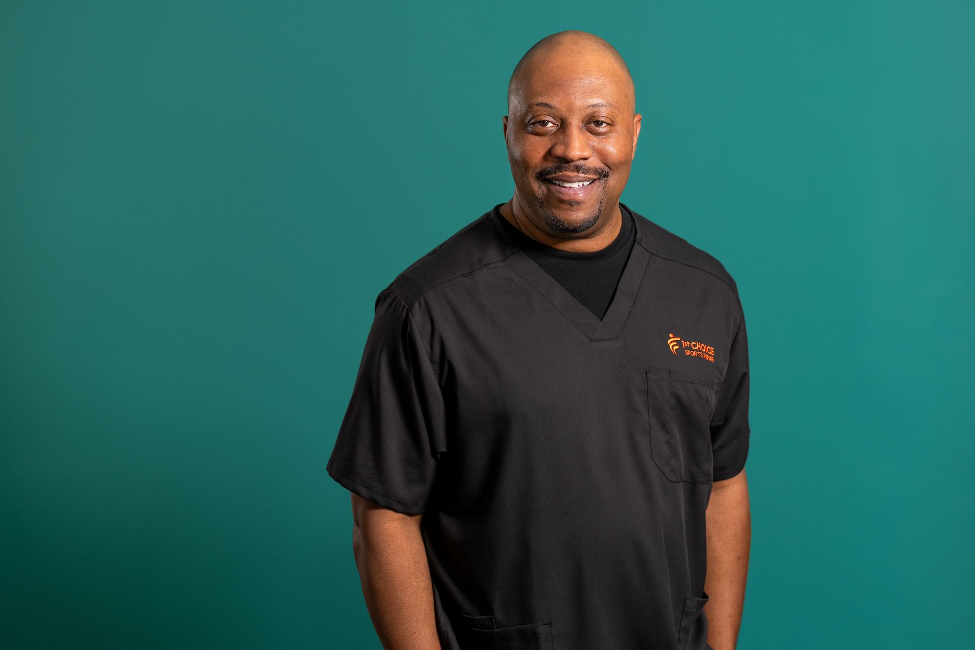 Man in black scrubs smiles against a teal background.