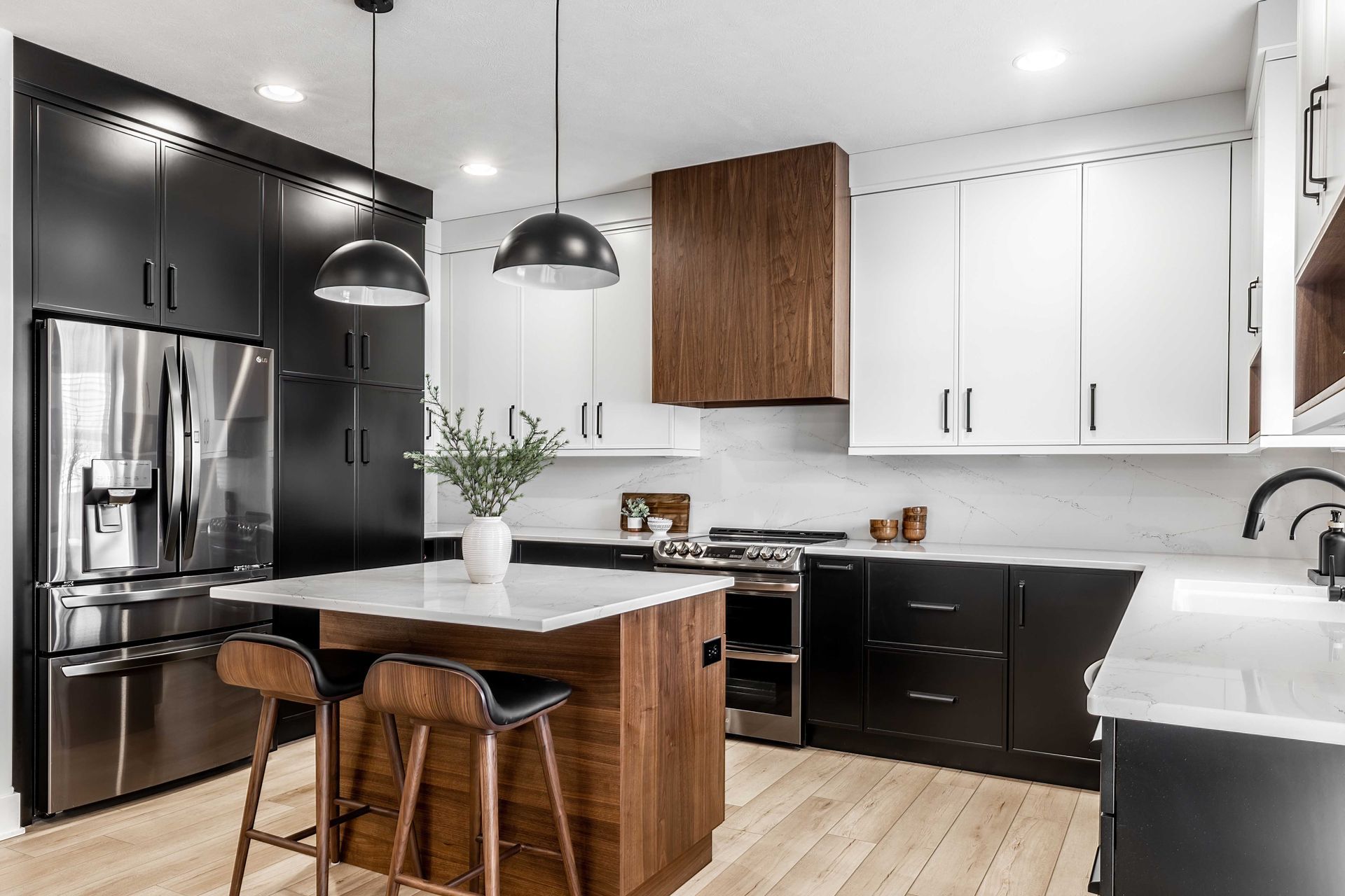 Cuisine moderne avec placards noirs et blancs, réfrigérateur en inox, îlot central et tabourets en bois.