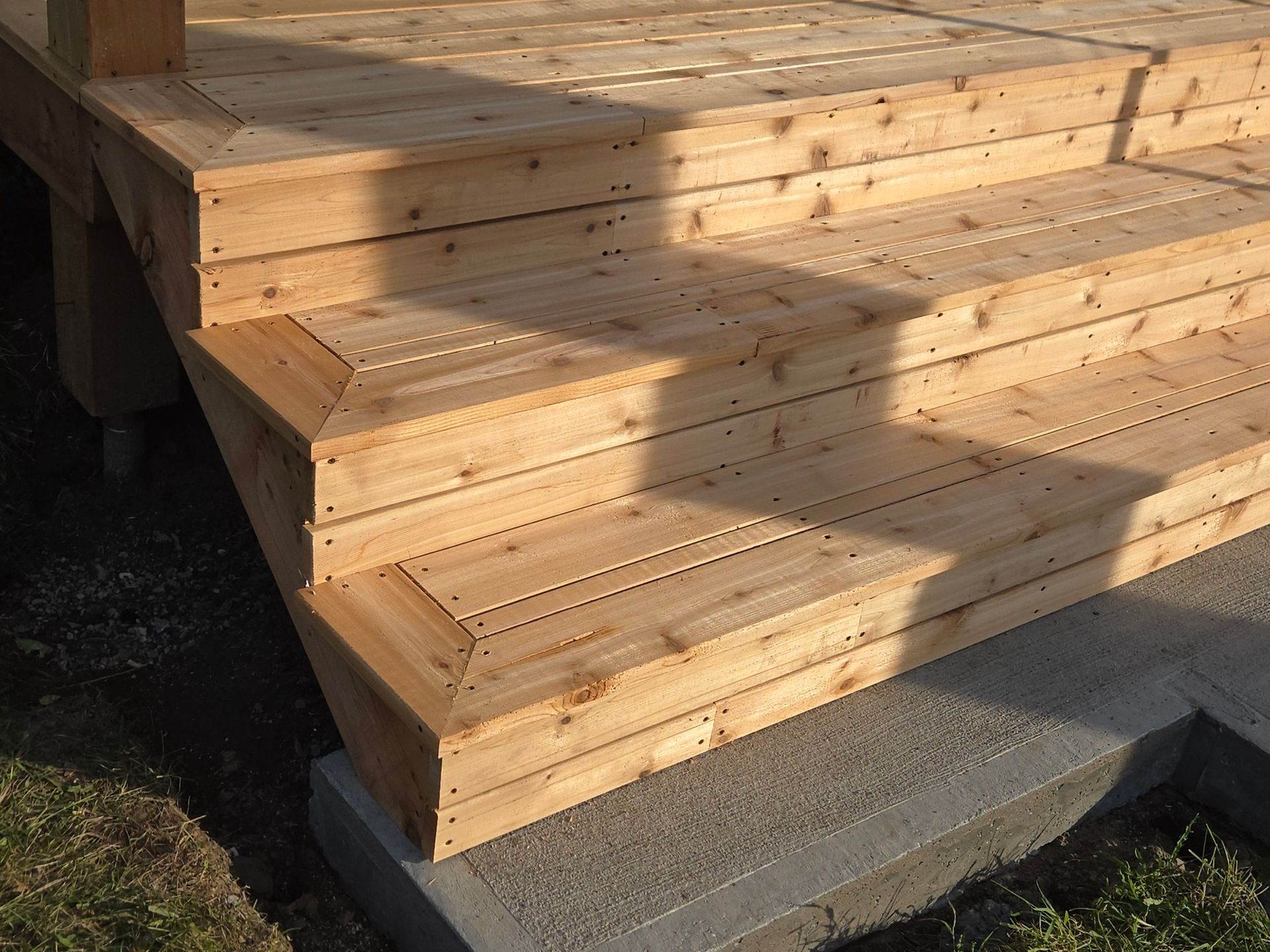 Des marches en bois mènent à une petite terrasse aménagée sur une dalle de béton.