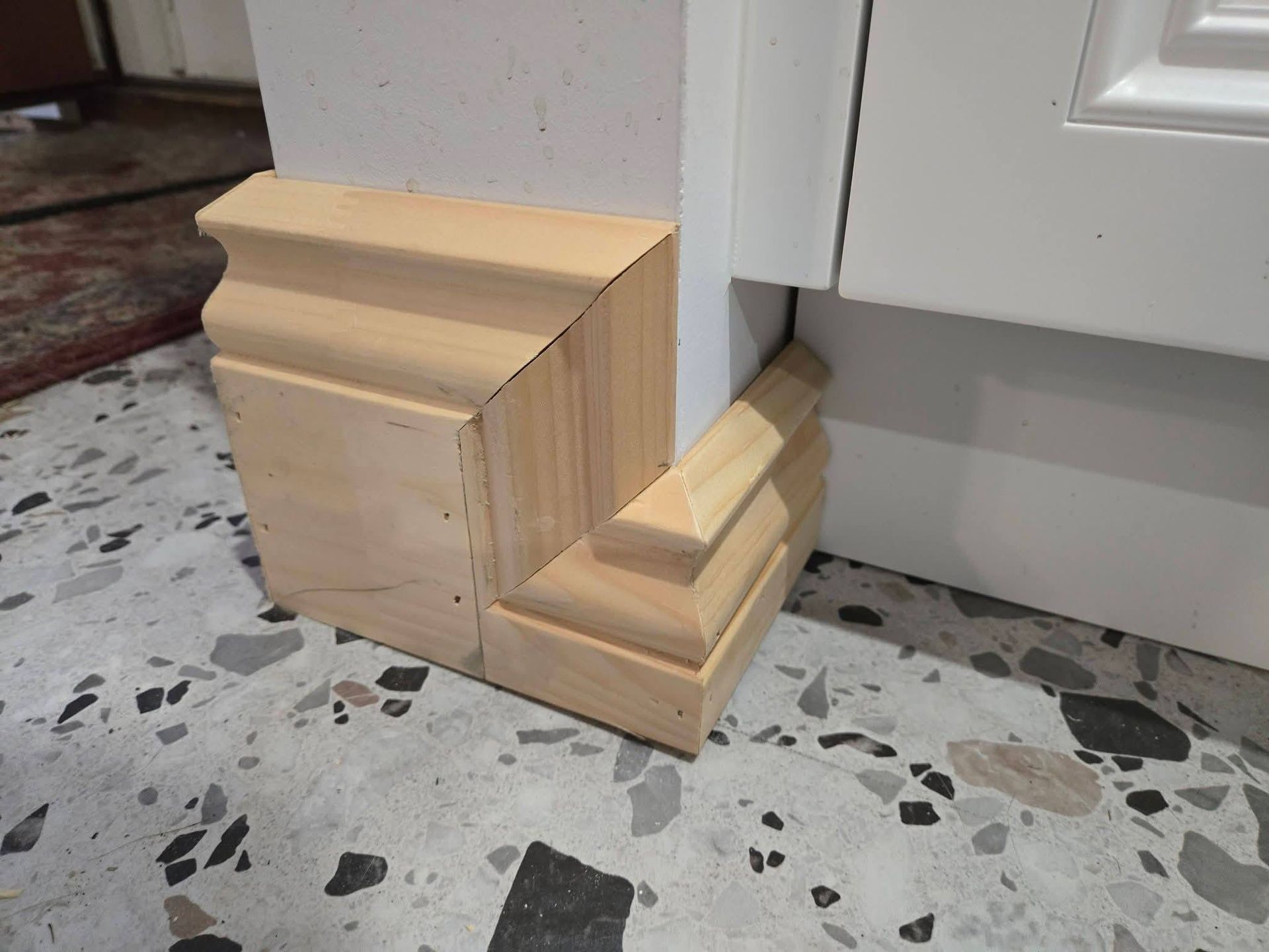 Échantillon de moulure décorative en bois dans une pièce, à côté d'une armoire blanche sur un sol moucheté