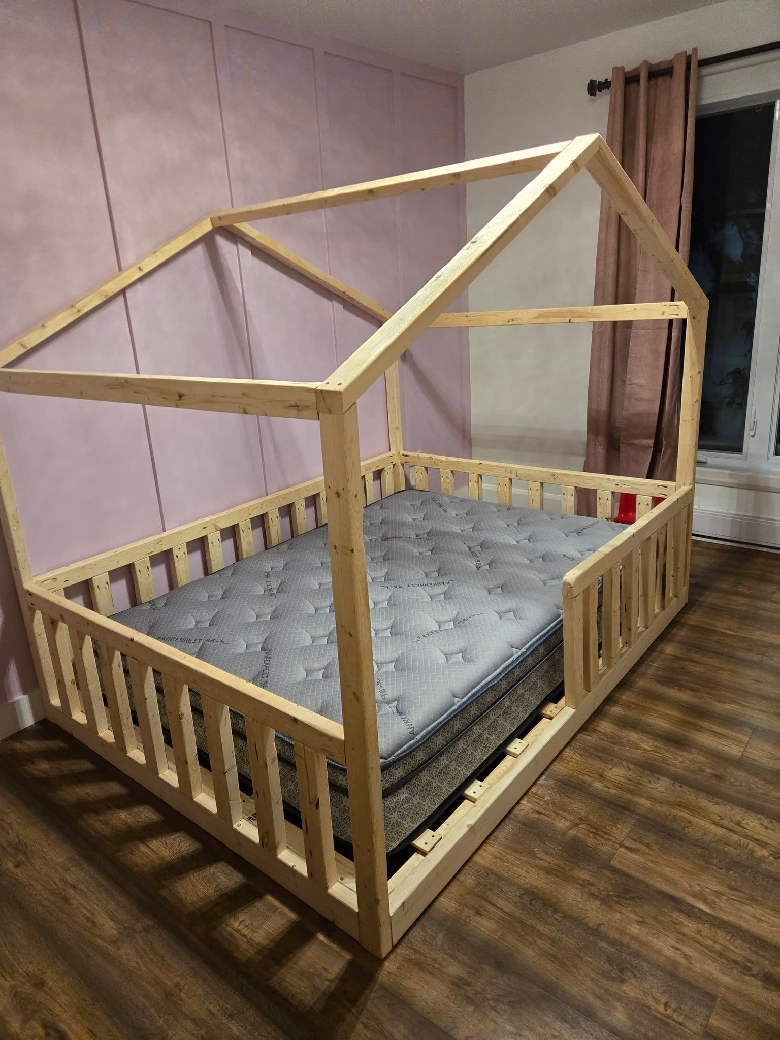 Cadre de lit en bois en cours de fabrication dans une chambre, avec un matelas gris et un toit inachevé.