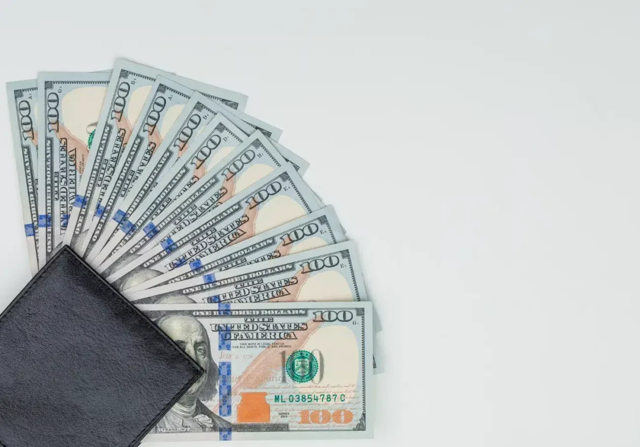 Black wallet fanned out with US $100 bills on a white surface.