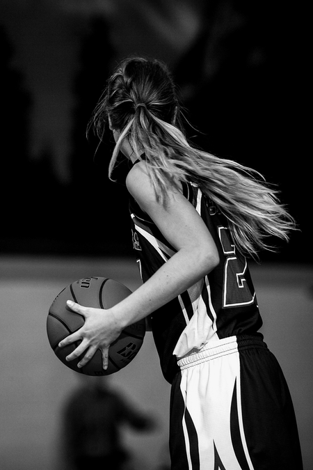 Basketball player in a dark uniform dribbling on court, viewed from the side.