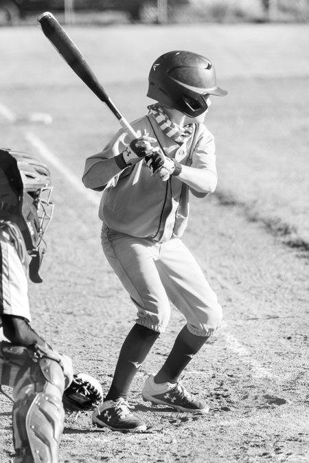 Young baseball player in a helmet swings a bat on a dirt field.