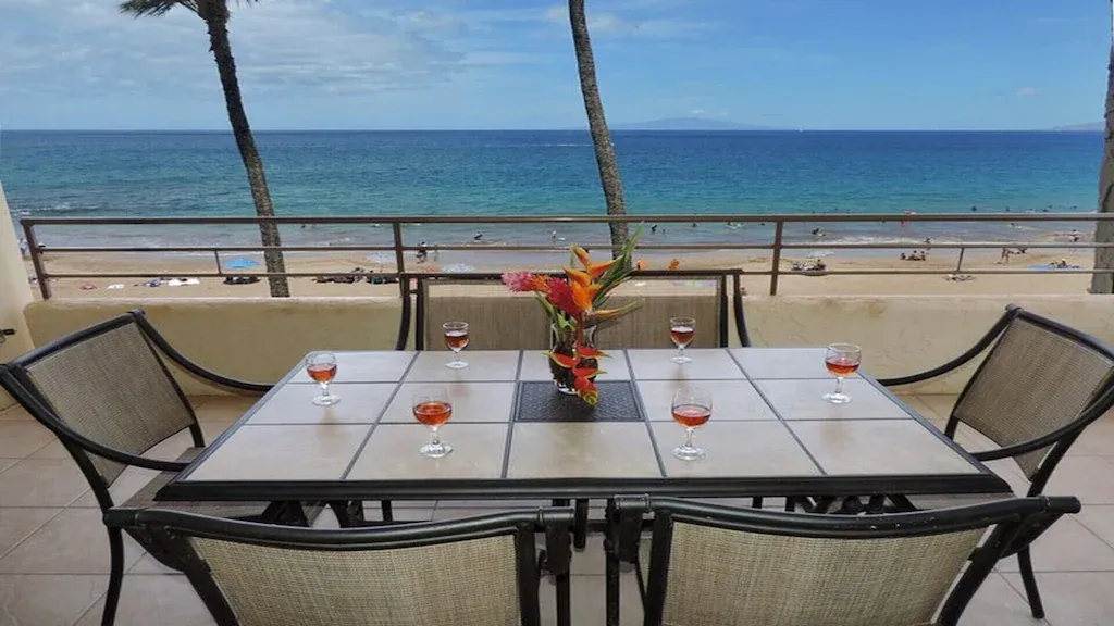 Balcony with table set for six, ocean view, wine glasses, flower arrangement.