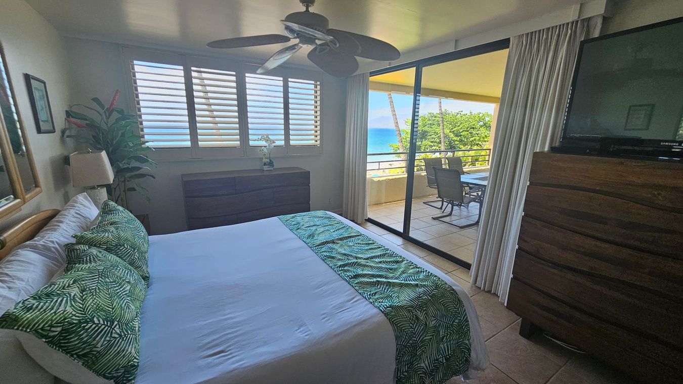 Bedroom with ocean view; bed with green patterned pillows, dresser, and sliding glass doors to a balcony.