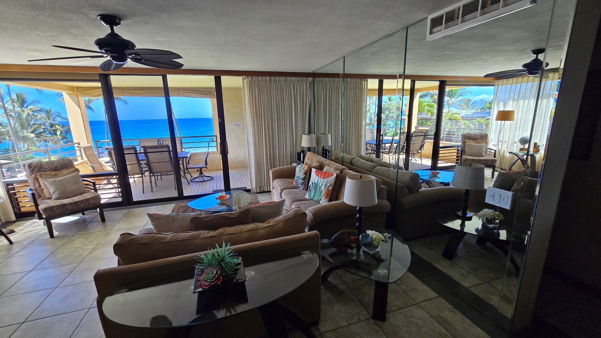 Living room with ocean view, brown furniture, large windows, and a mirrored wall.