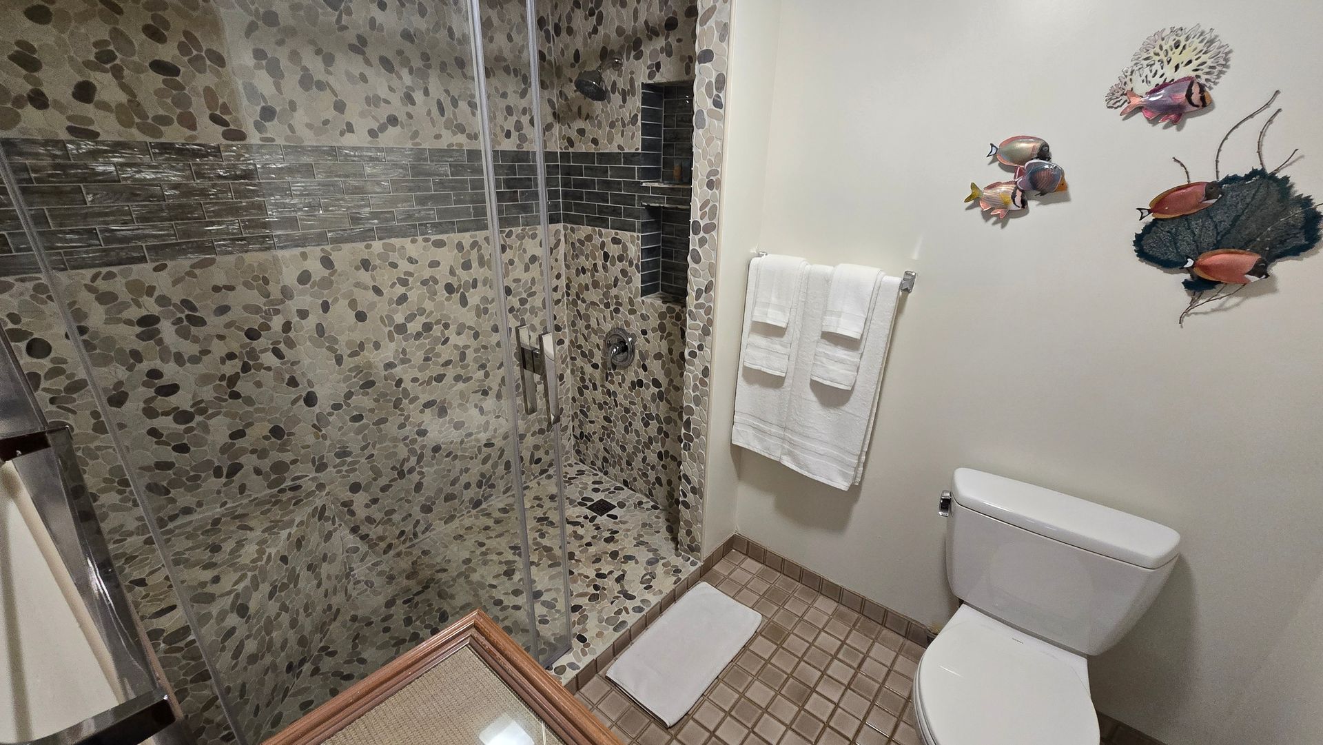 Bathroom with pebble-tiled shower, white toilet, wall art, and a towel rack with folded towels.