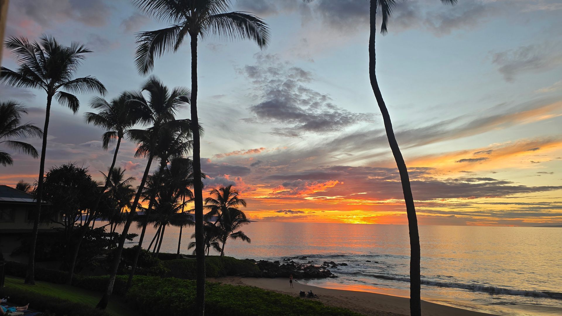 Palm trees silhouetted at sunset over a calm Polo beach with orange and pink sky reflections on the water