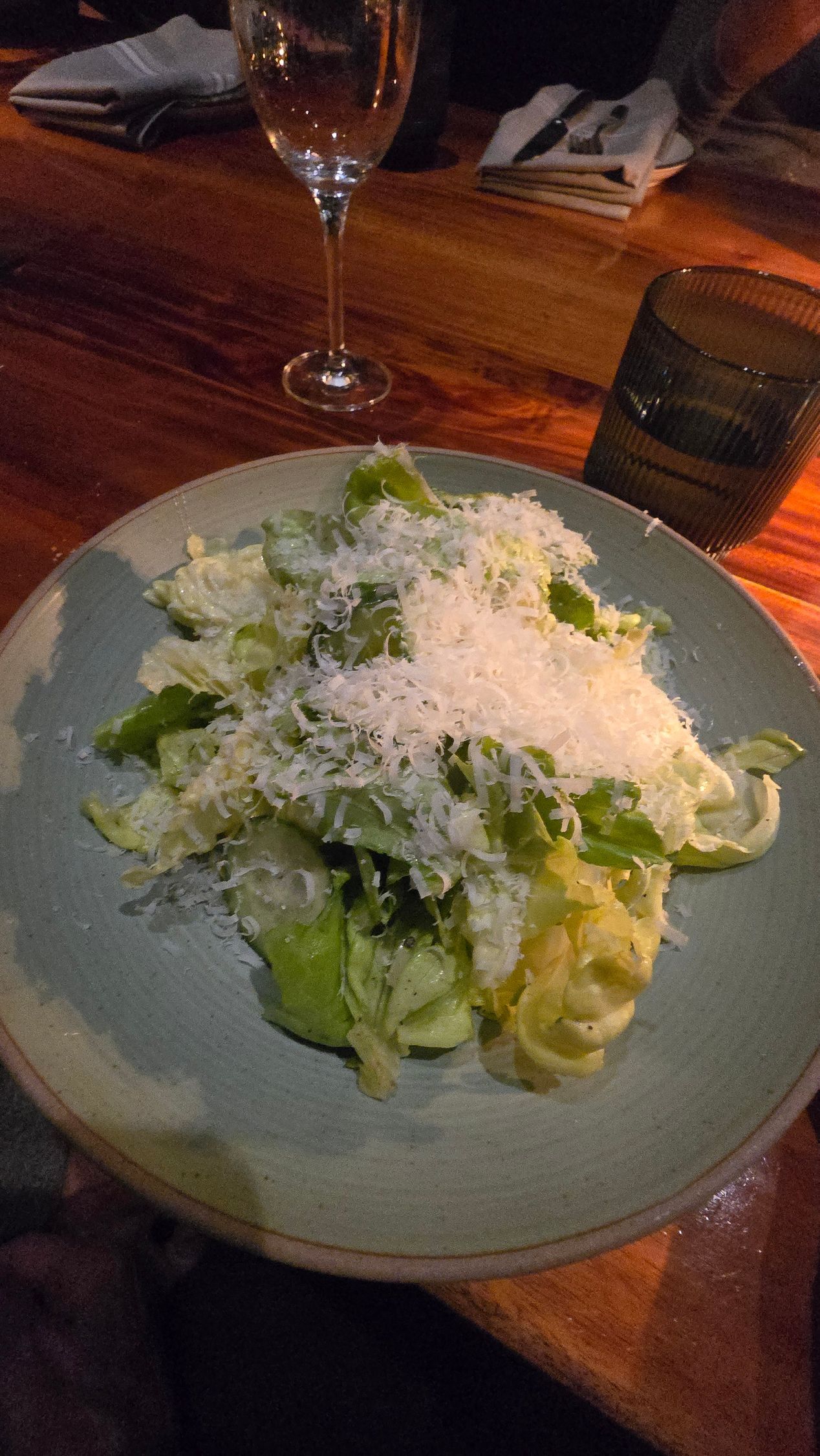 Caesar salad on a blue plate on a wooden table, with wine glasses nearby.