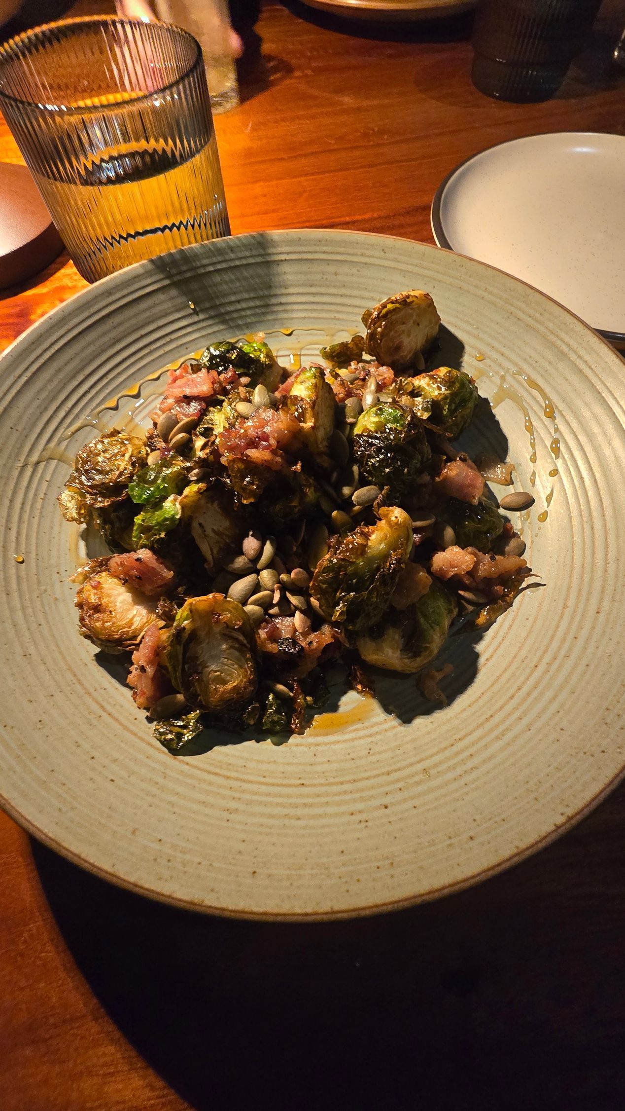 Plated roasted meat topped with herbs on a white dish, on a wooden table beside a drink.