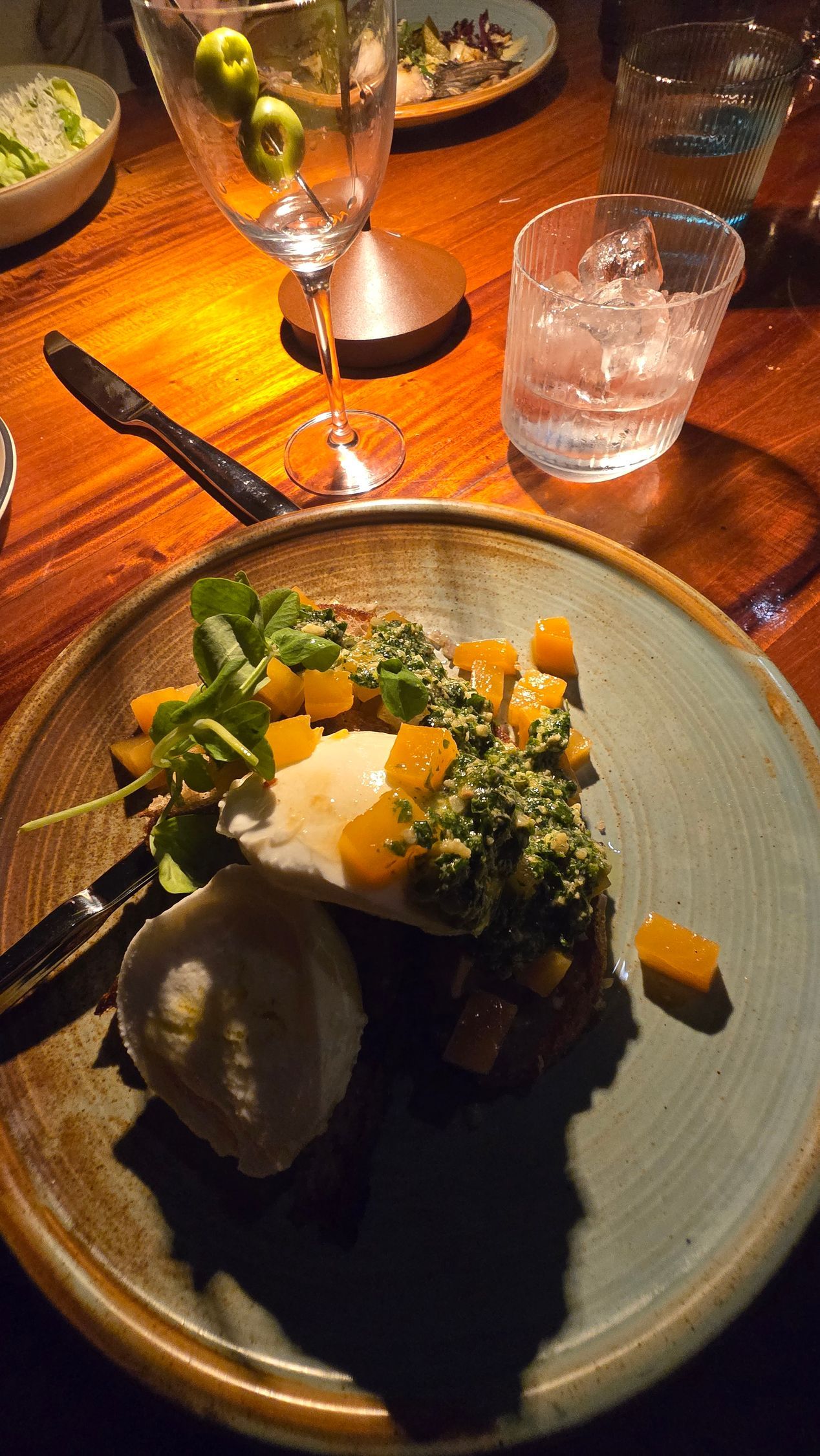 Plated gourmet dish with greens and sauce on a restaurant table beside a candle and water glass