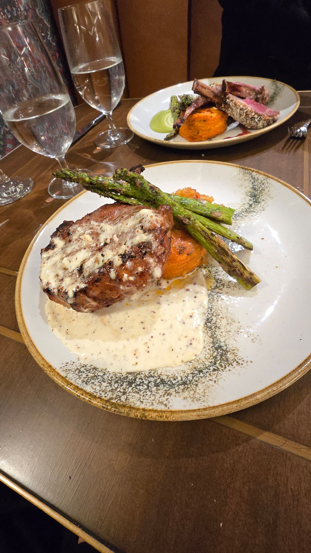Plated gourmet fish with sauce and asparagus on a table, with another dish in the background.