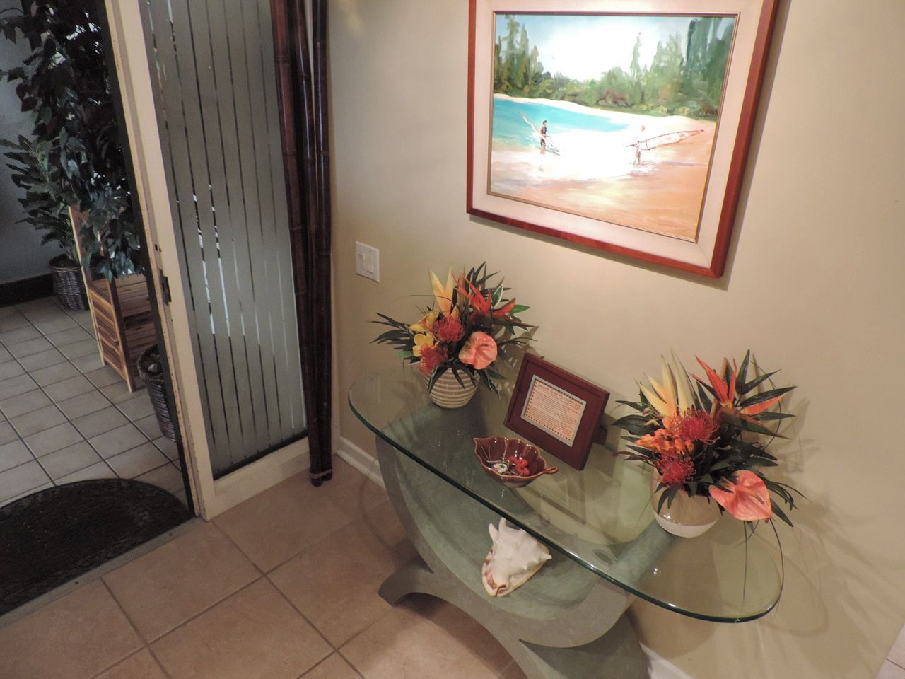 Entryway with glass table, floral arrangements, framed artwork of beach scene.