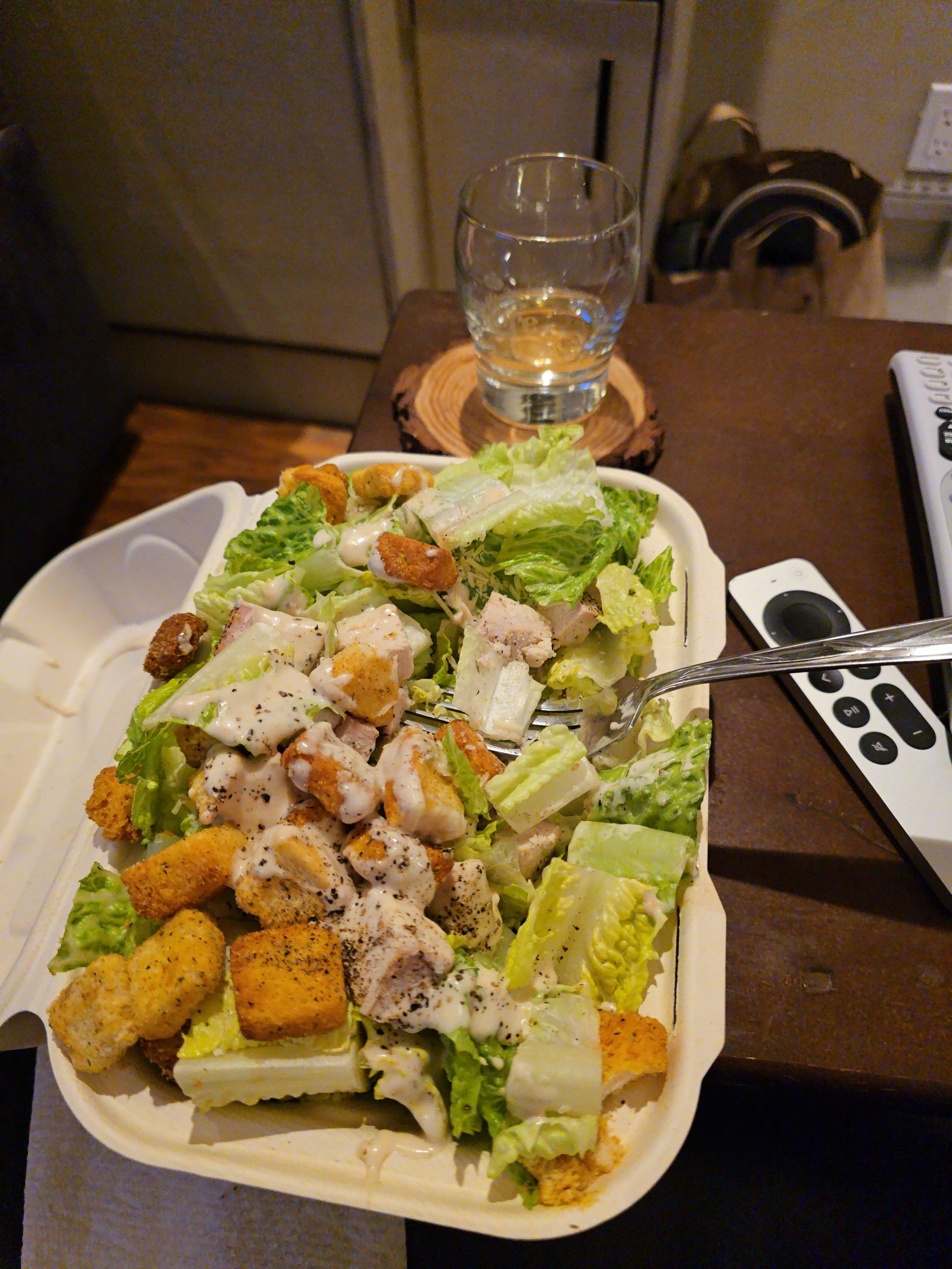 Caesar salad with croutons and shaved cheese on a table beside a glass of water