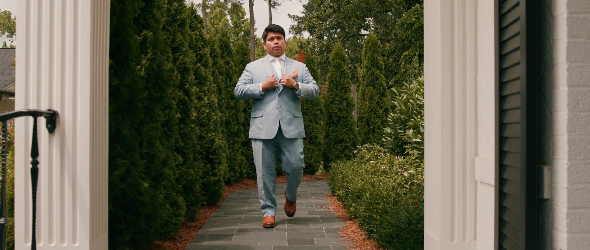 Man in a light blue suit adjusting his jacket while walking down a brick path.