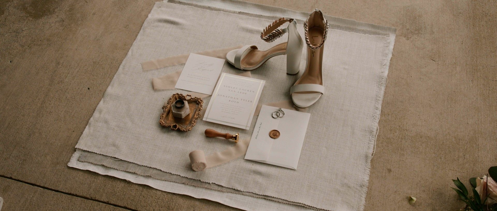 Wedding details arranged on a textured surface: white heels, stationery, wax seals.