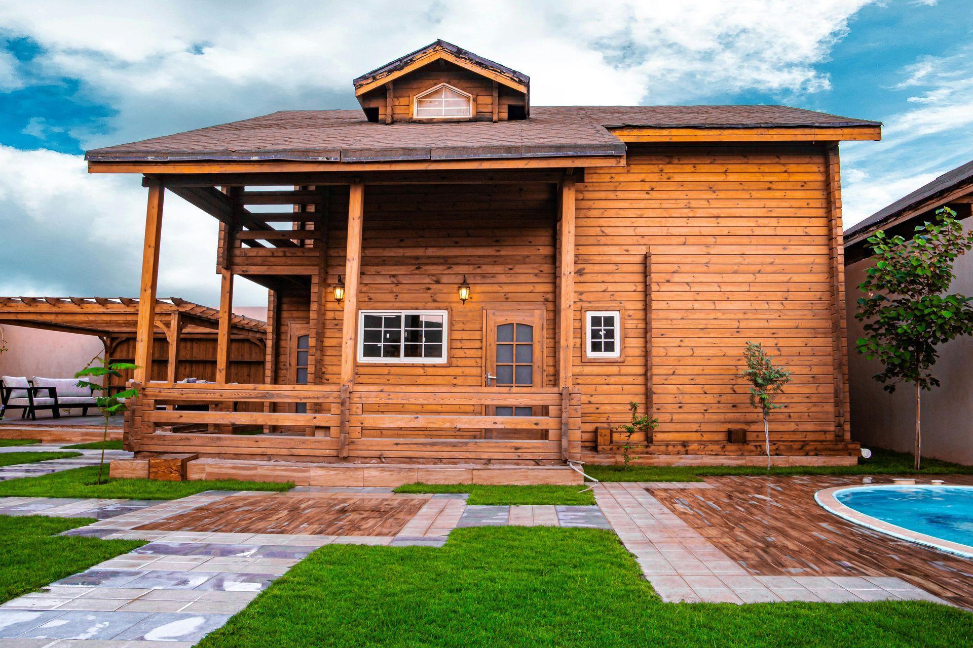 Wooden cabin-style house with porch, small windows, and a yard with grass and pool.