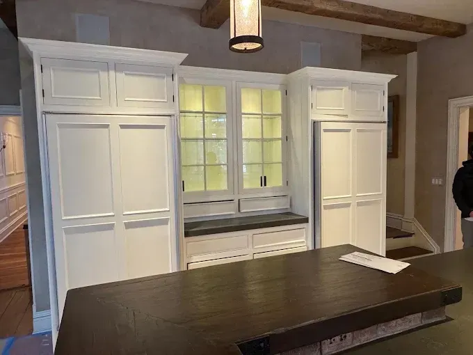White built-in cabinets and a windowed hutch behind a dark wood island in a kitchen.