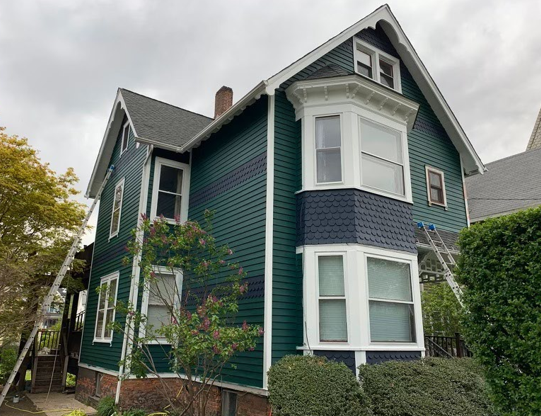 Green Victorian-style house with white trim and dark blue accents on a cloudy day