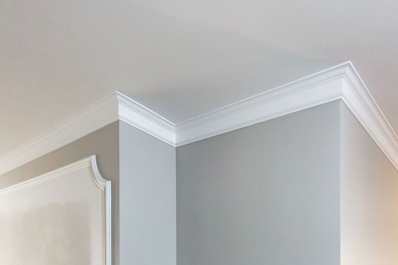 Light gray interior wall corner with white crown molding and door trim on the left
