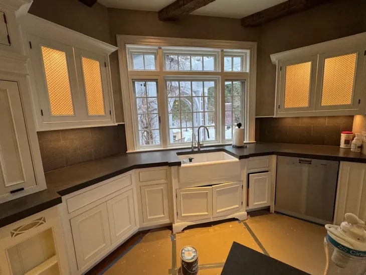 Bright kitchen with white cabinets, dark countertops, large window, and stainless dishwasher.