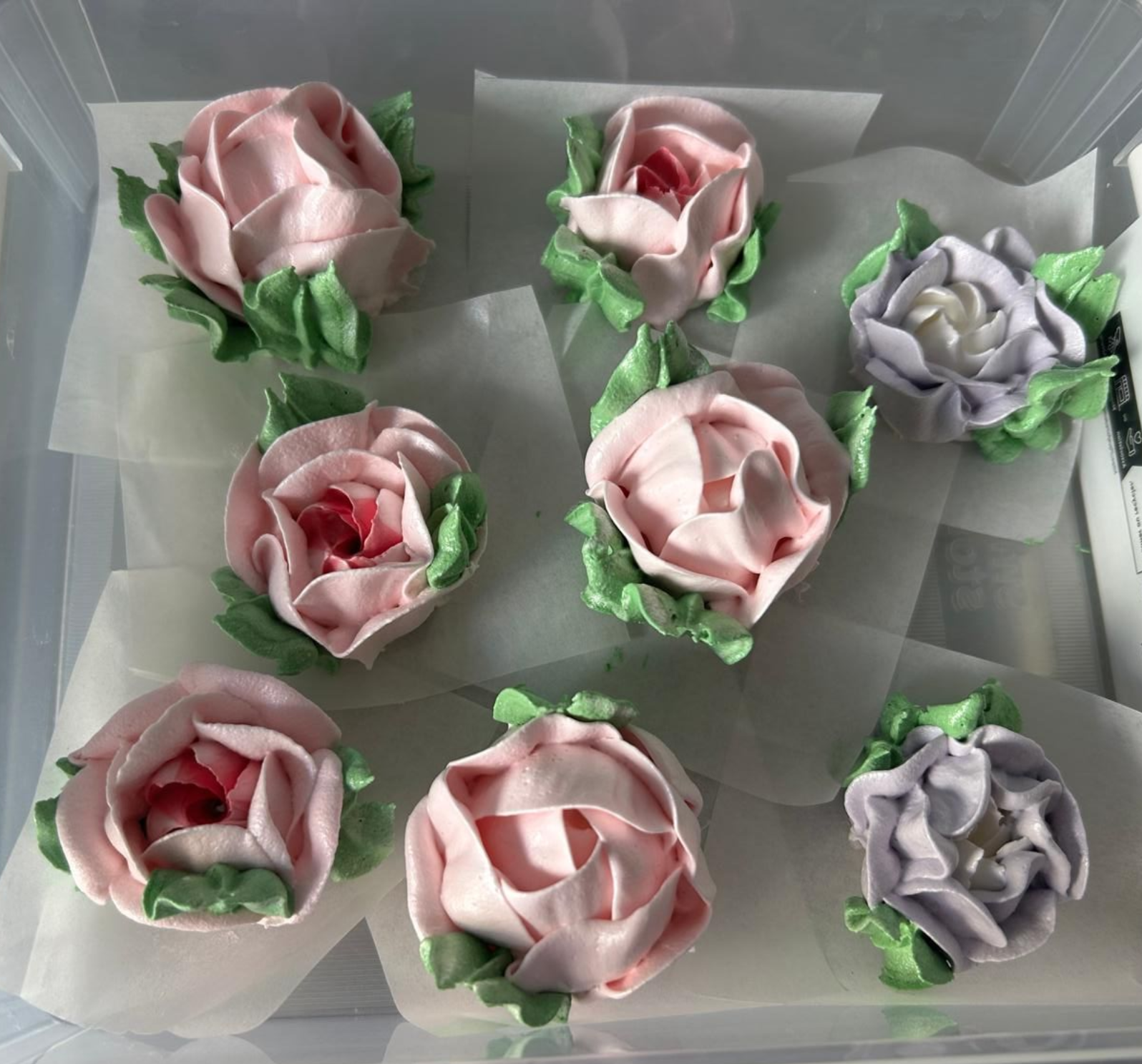Verschiedene rosa und lavendelfarbene, blütenförmige Leckereien, in einer Schachtel auf weißem Seidenpapier arrangiert.