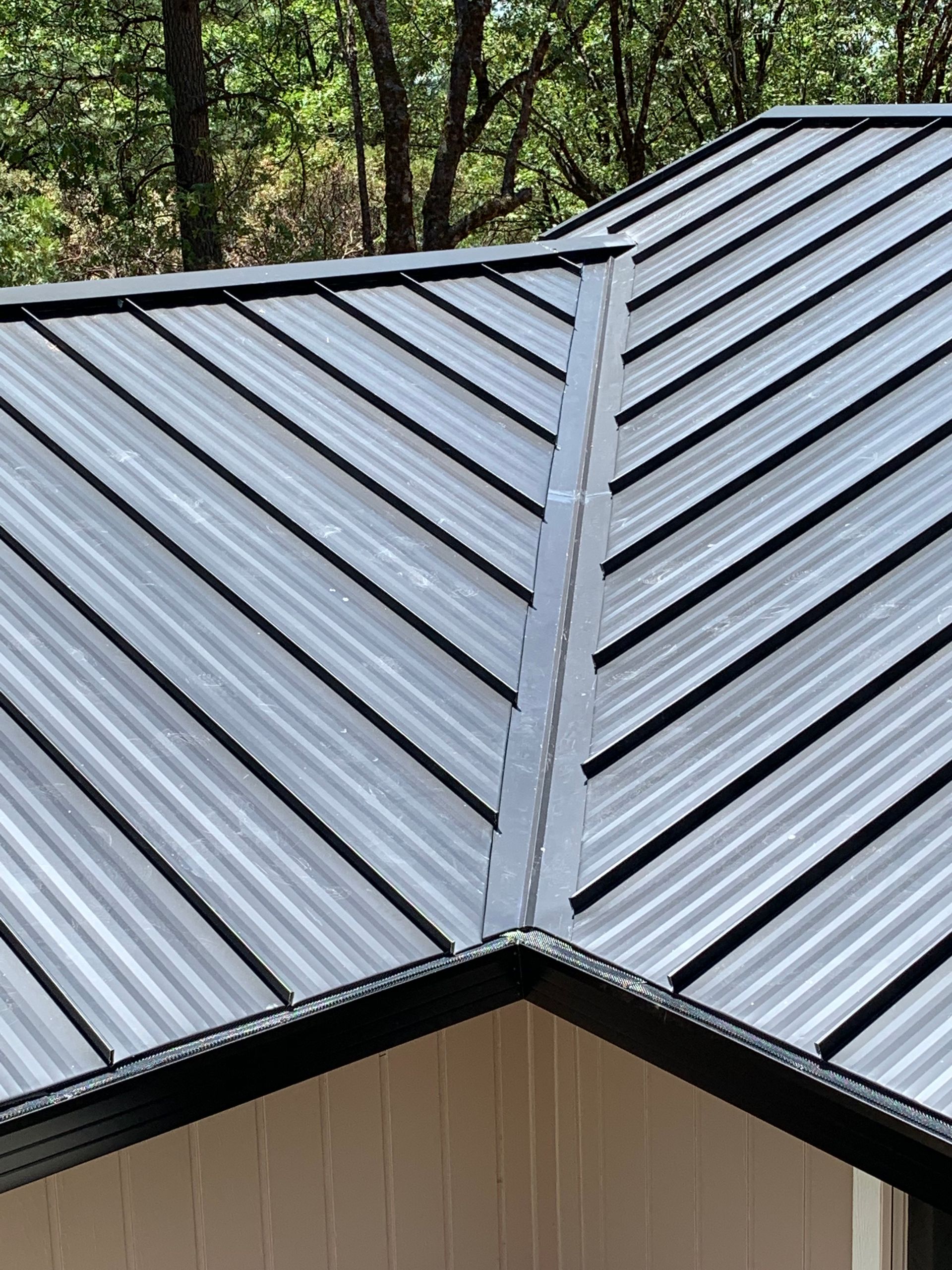 A close up of a metal roof on a house with trees in the background.