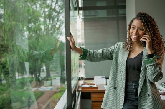 A woman is standing in front of a window talking on a cell phone.