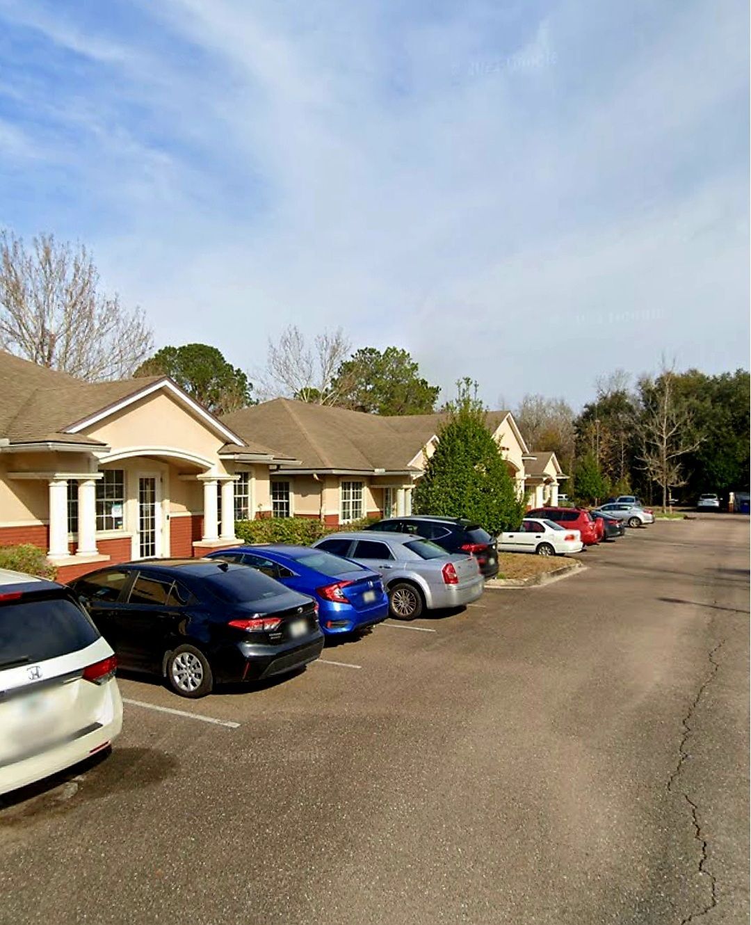 Cars parked in front of beige single-story buildings under a blue sky.