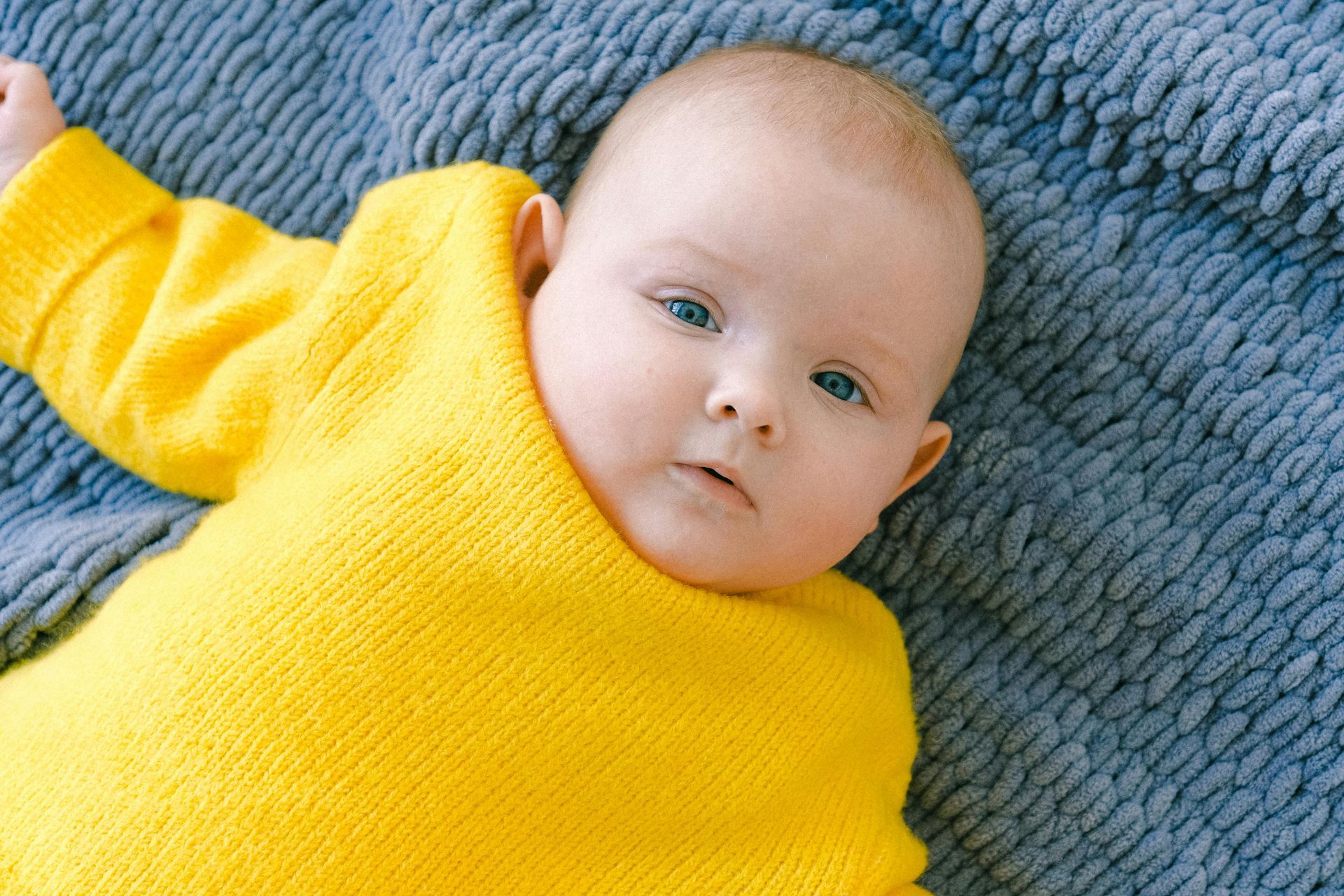Baby in yellow sweater on blue blanket.