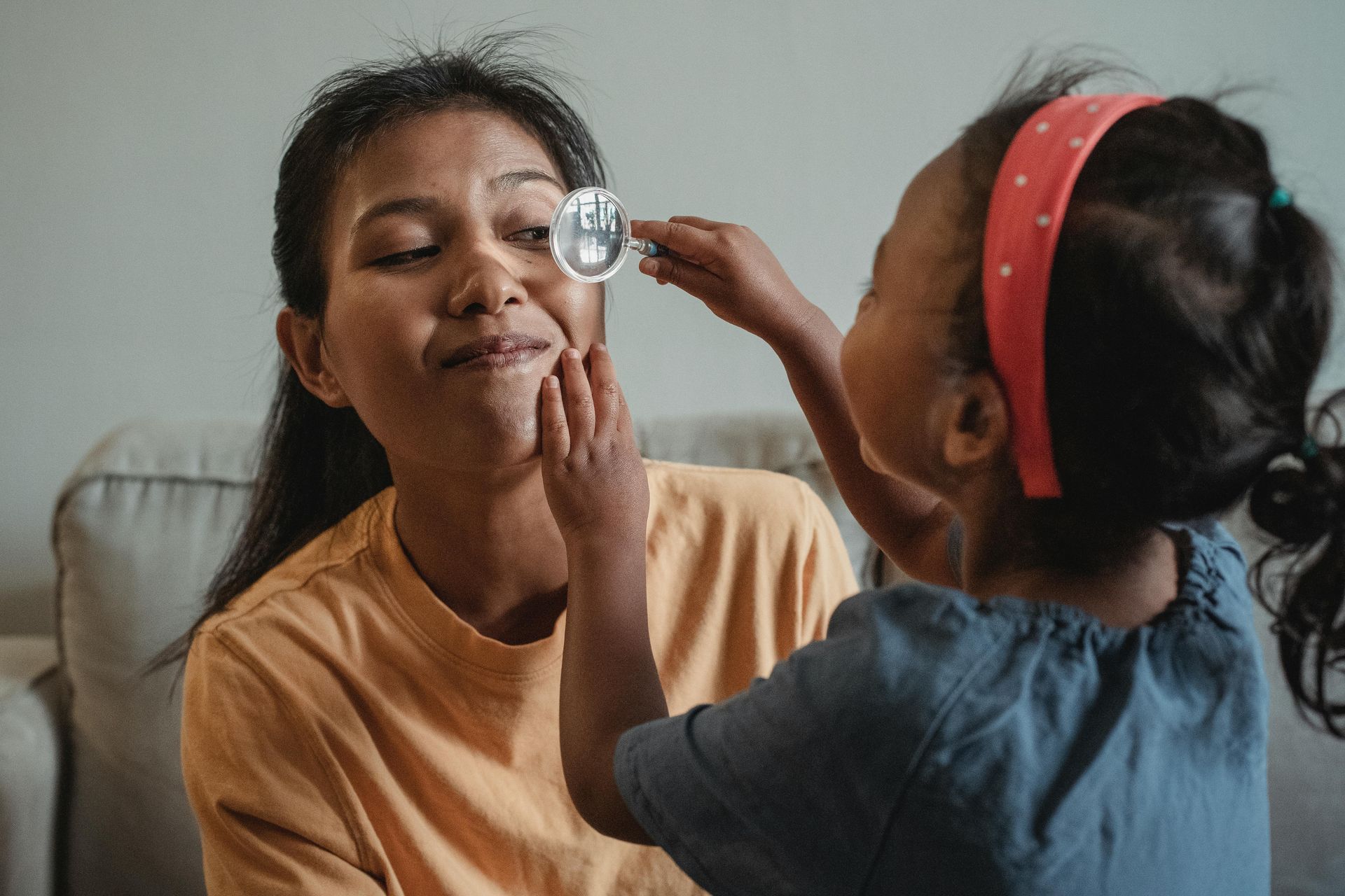 Child holding a small object to parent's face, possibly playing, indoors.