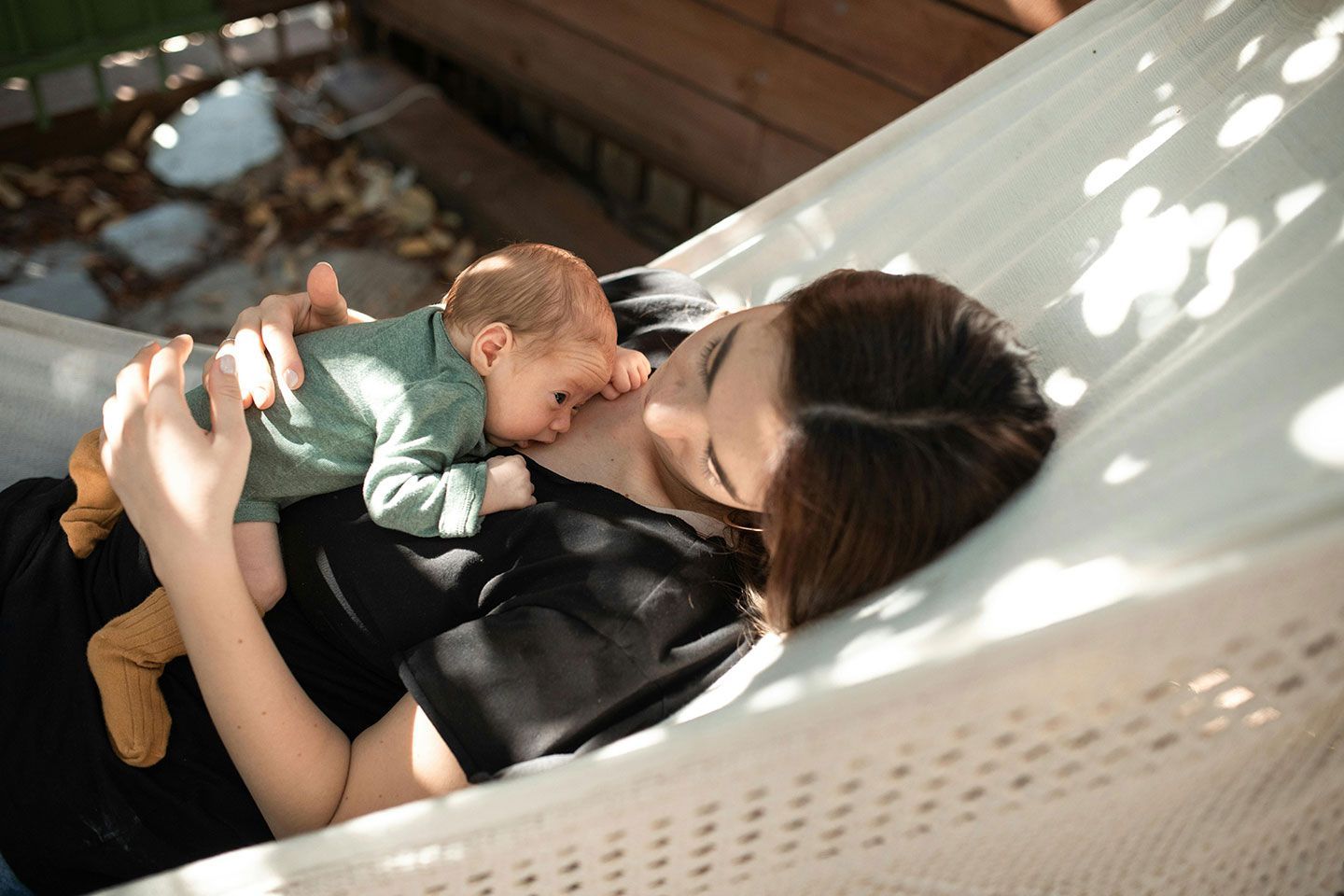 Woman holding a baby in a hammock outdoors, enjoying a sunny day.