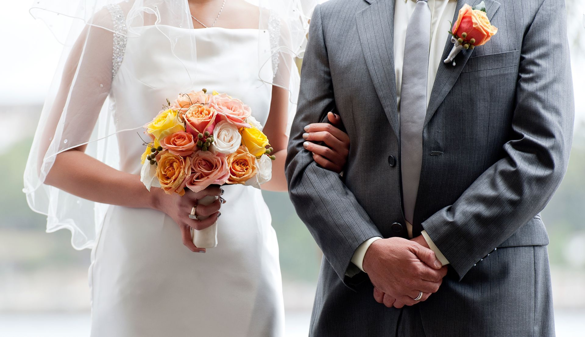 Bride and groom at a wedding, the bride in a white dress with a bouquet, the groom in a grey suit.