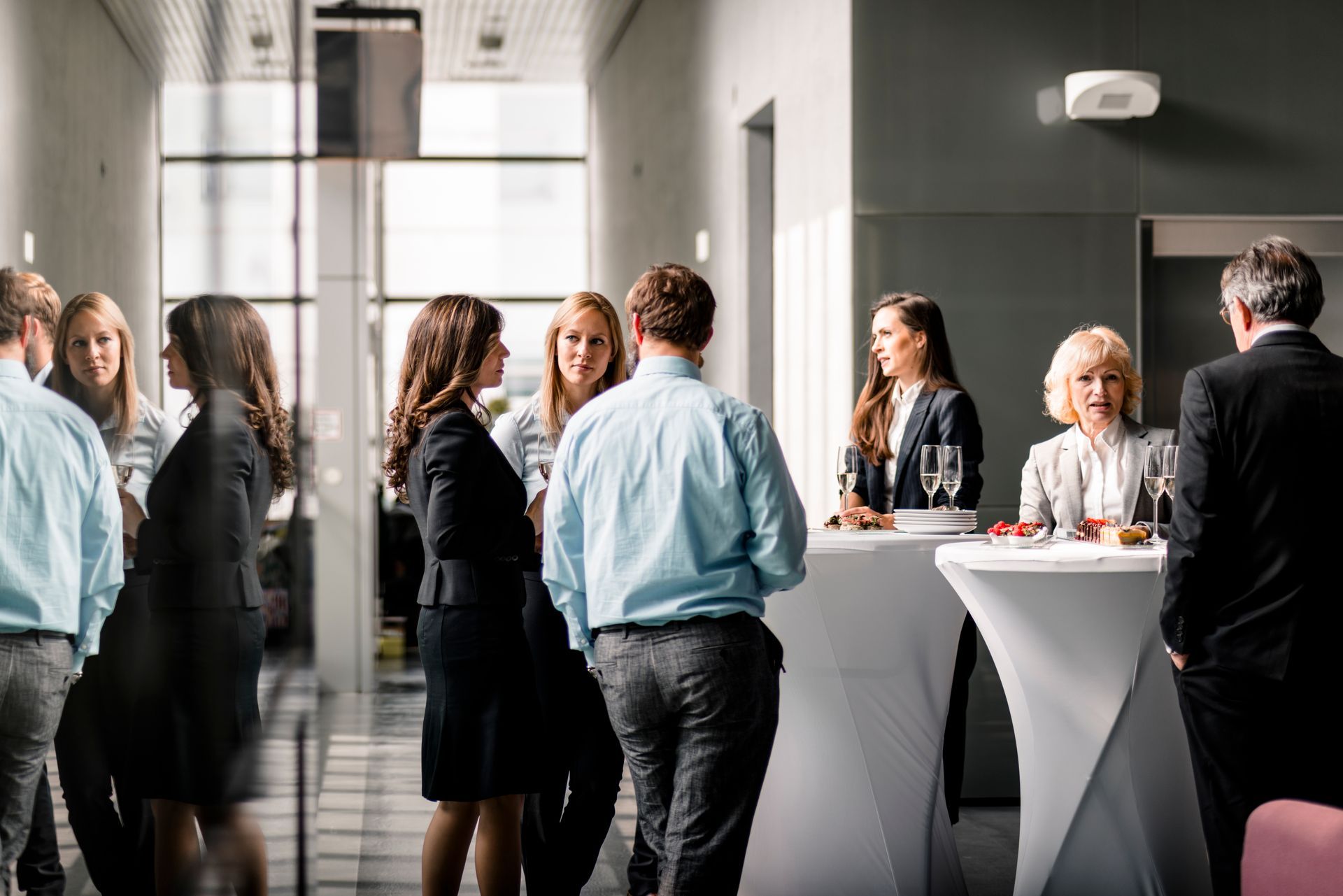People in business attire at a networking event, conversing near high-top tables.