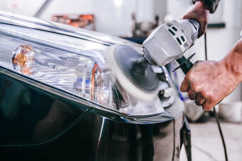 Meccanico che lucida un faro di un'auto con una lucidatrice elettrica