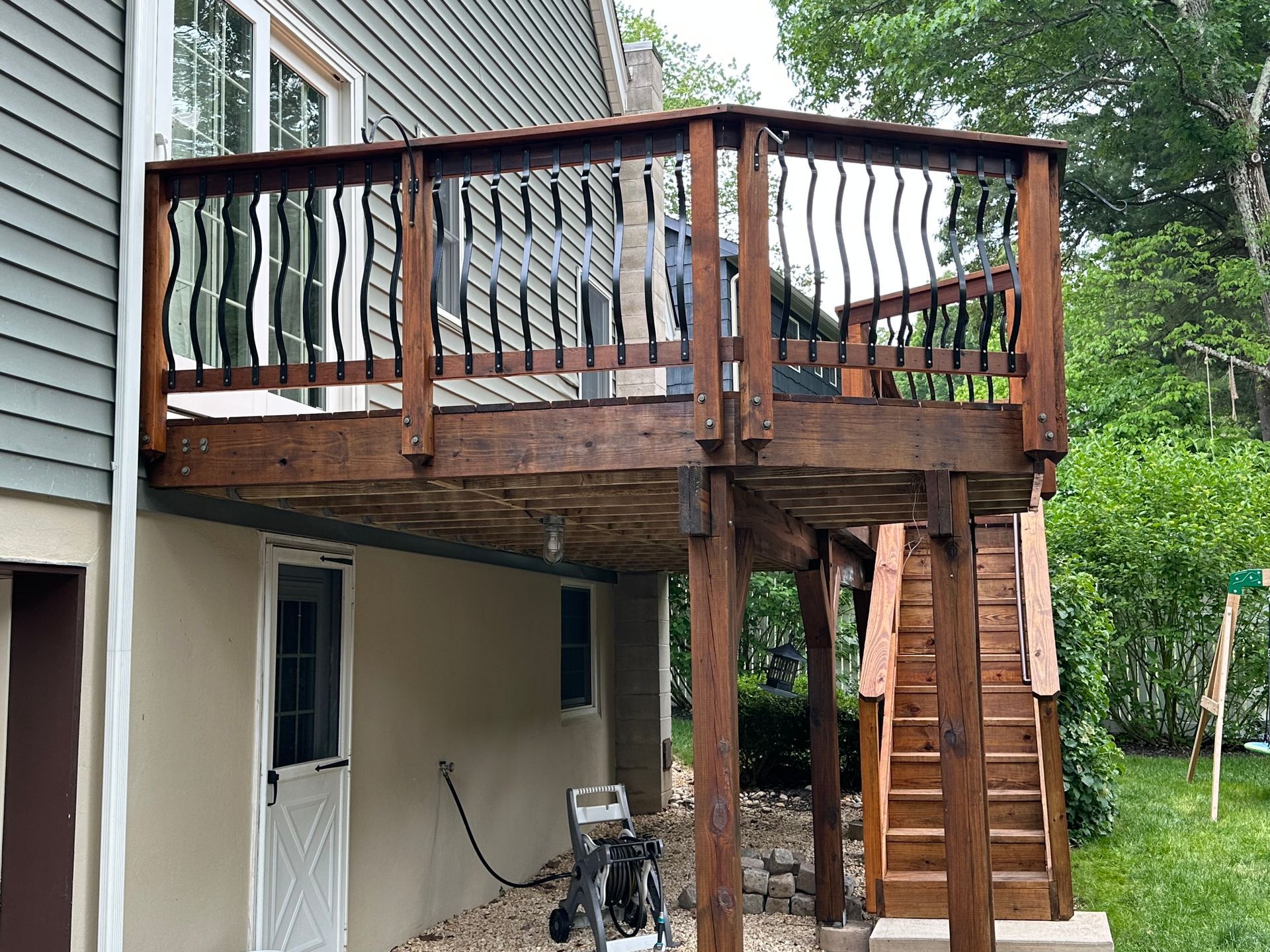 Wooden elevated deck with stairs attached to a house, overlooking a grassy yard