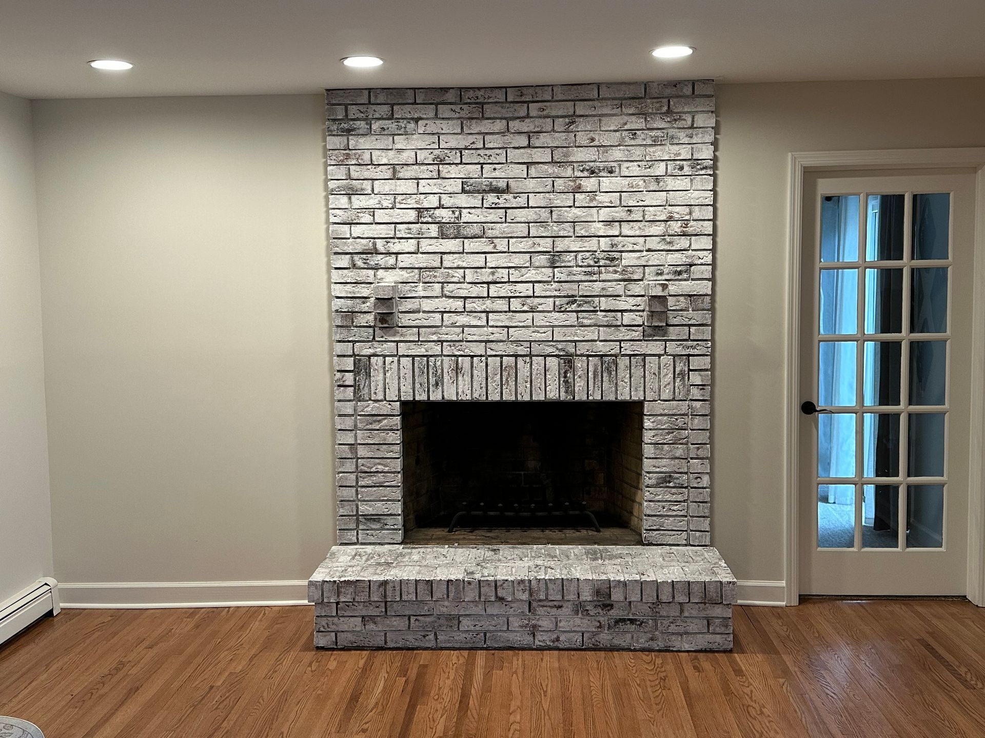 Living room with white brick fireplace, wood floor, recessed lights, and a glass door on the right.