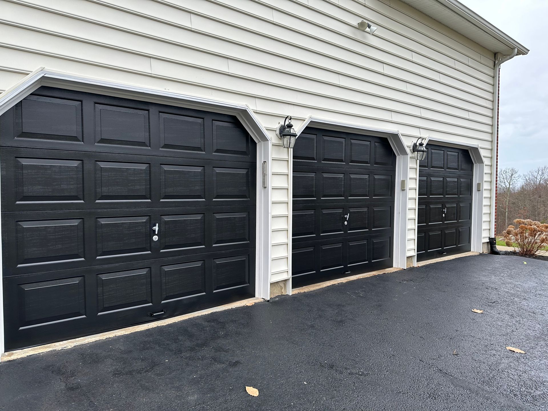 A garage with three black garage doors and a white siding.