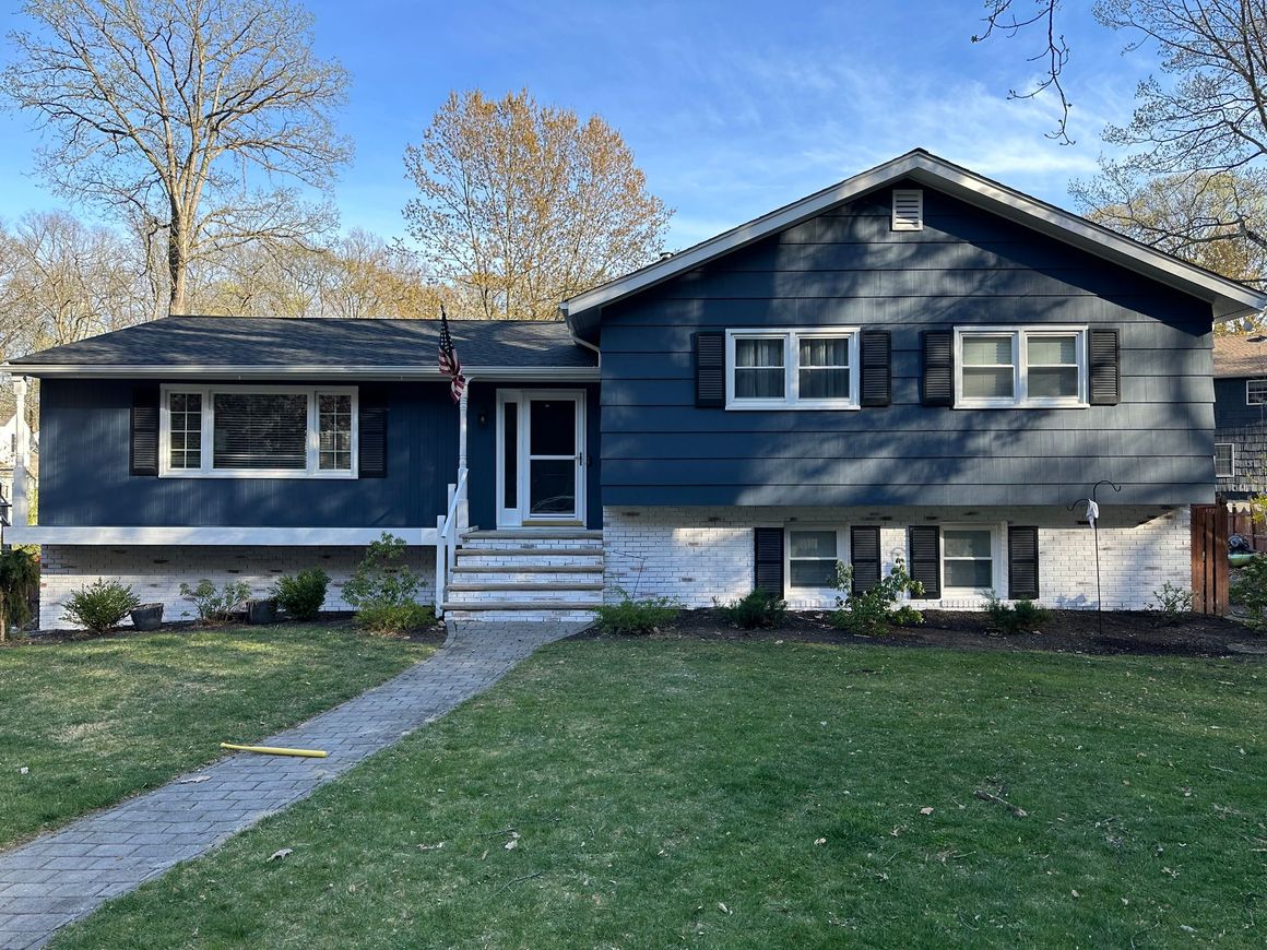 A blue house with white trim and shutters is sitting on top of a lush green lawn.
