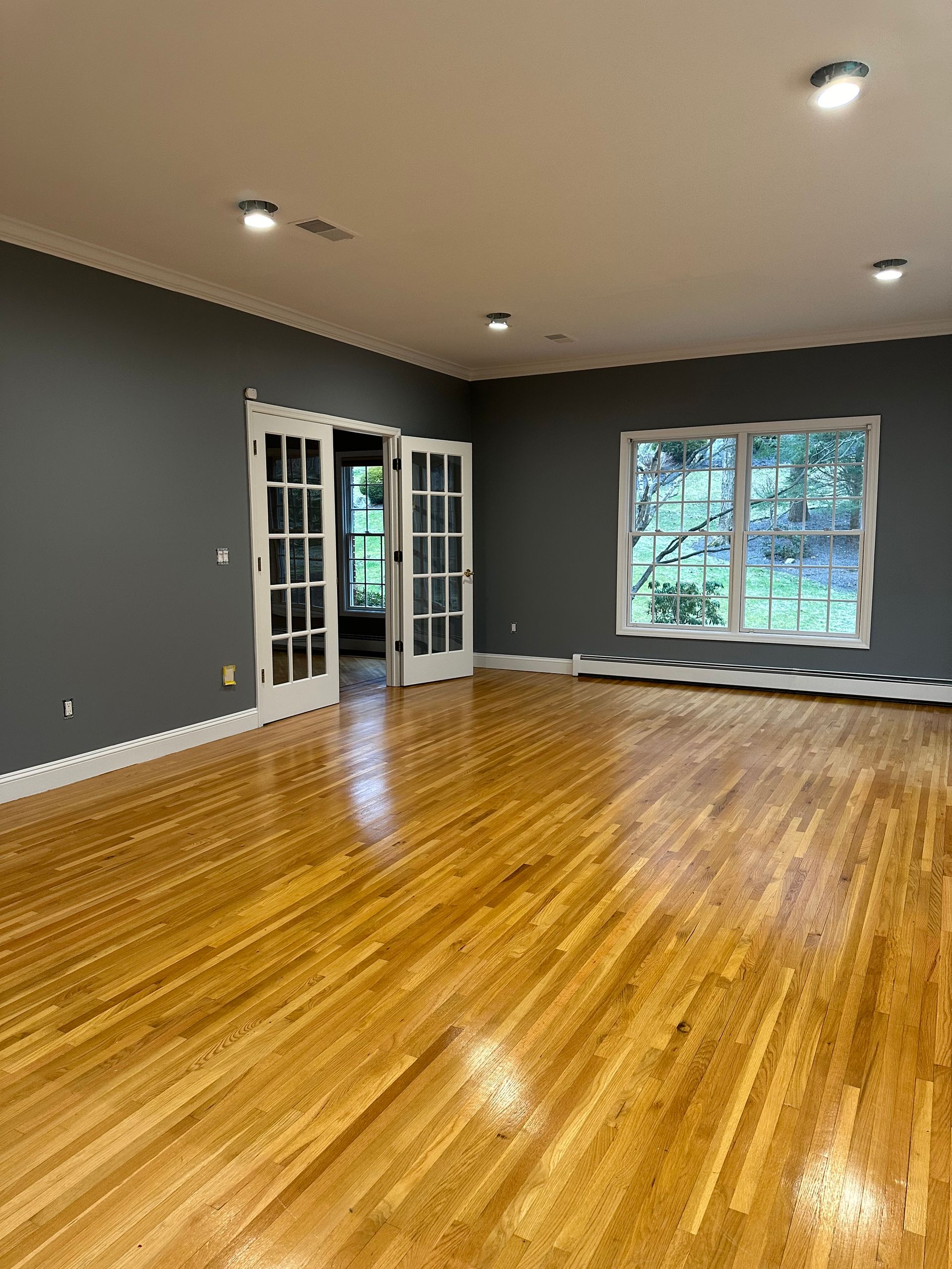 An empty living room with hardwood floors and gray walls.