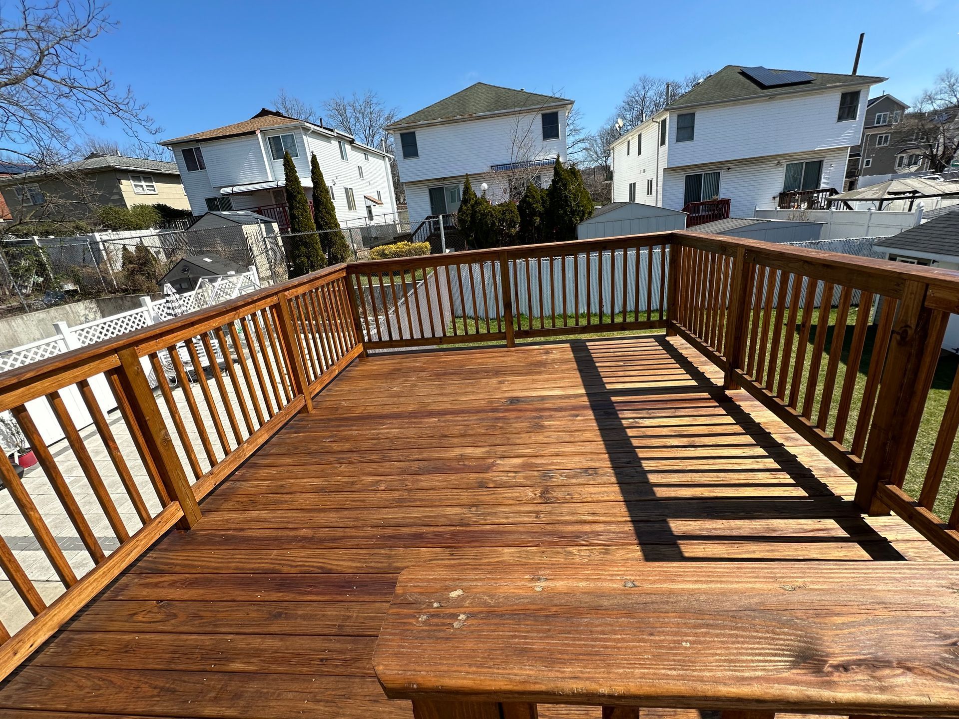 A wooden deck with a railing in the backyard of a house.