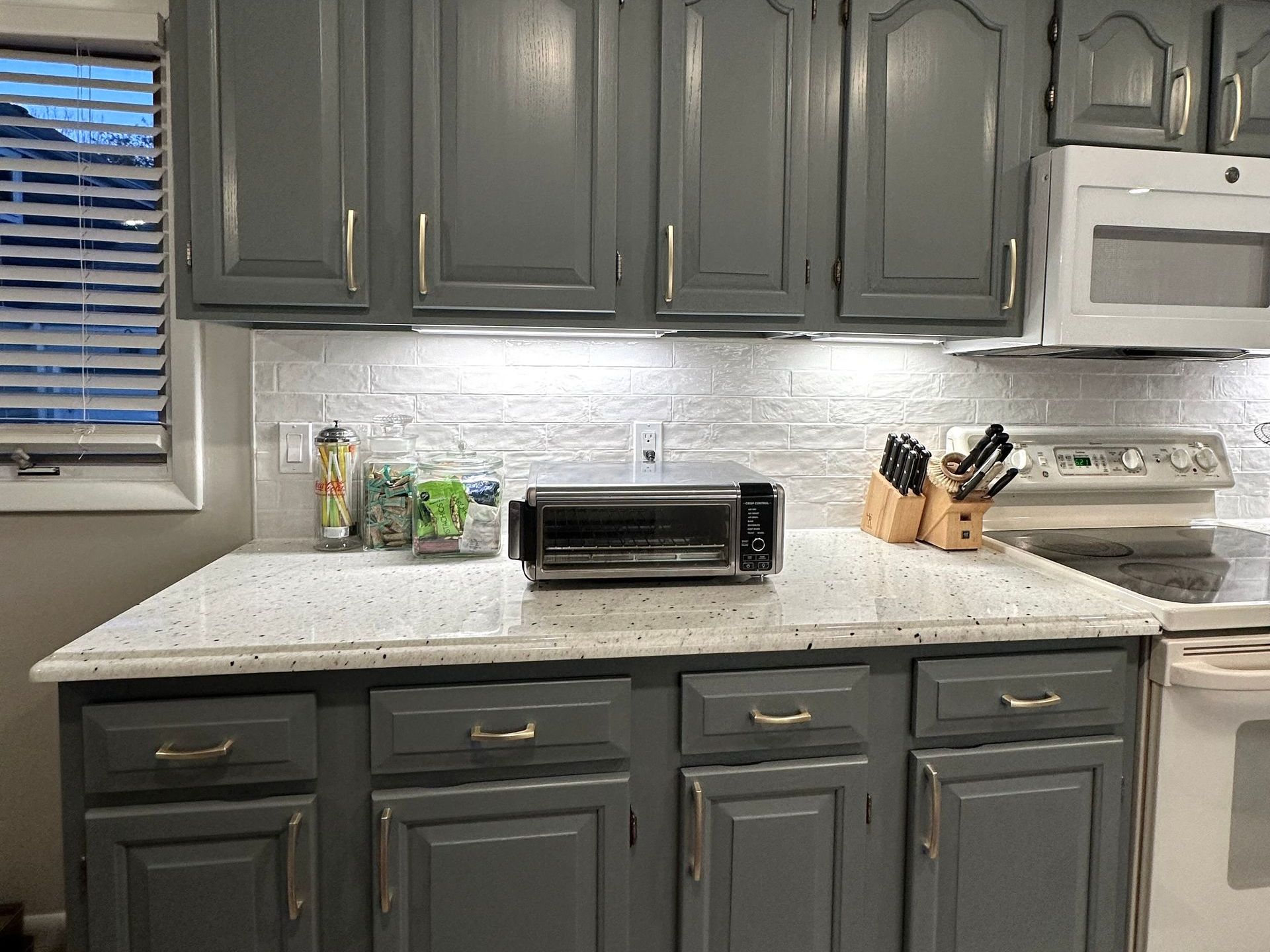 A kitchen with gray cabinets , white appliances , a toaster oven and a microwave.