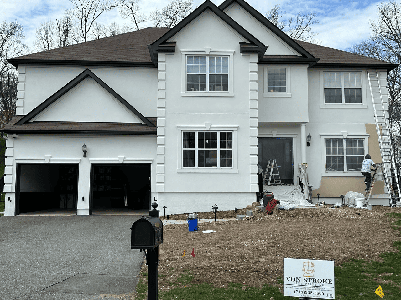A large white house with a brown roof is being painted