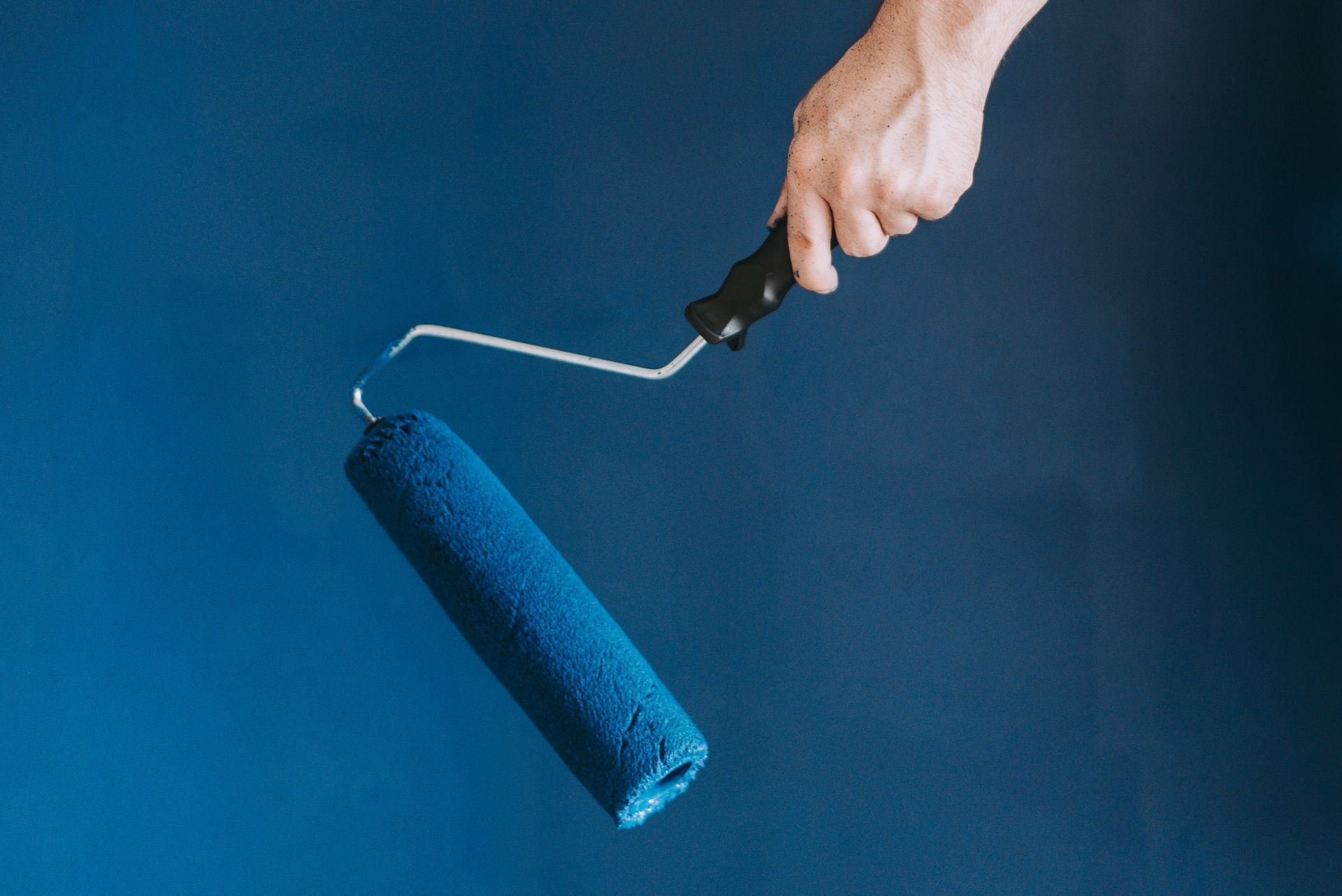A person is holding a blue paint roller in their hand.